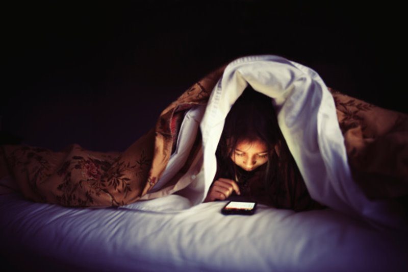 Mujer revisando su celular en la cama